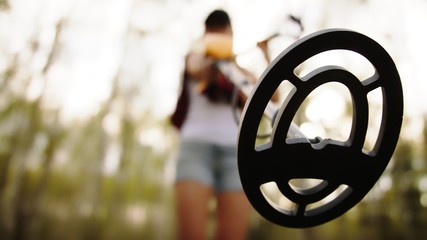 Young woman archeologist using metal detector in the forest. Low angle view. High quality photo