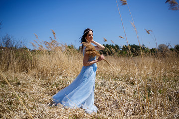 Portrait of a tender girl in a blue long dress in dry peas with a smile on her face on a sunny warm...