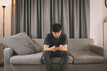 Young man sit down on the sofa while using mobile phone and drink coffee  relaxing at home