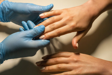 Hygiene, manicure and hand care. Nail cleaner and hand massage with oil from masseur. Manicurist wearing protective gloves keeping female hands with nails polish in manicure salon. Hands close-up. 