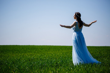 Fototapeta na wymiar Young woman in a blue long dress on a background of green field. Fashion portrait of a beautiful girl with a smile on her face