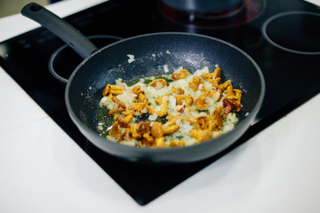 a frying pan on the stove in which mushrooms and onions are fried