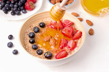 Healthy summer breakfast. Oatmeal porridge with fresh berries, almonds and honey on a white plate
