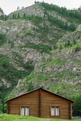 Fototapeta na wymiar A log wooden house with a lawn against the backdrop of a high mountain. Rest away from the city. Vacation. Rustic look. Summer tourism concept.
