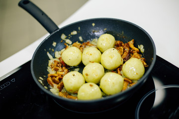 a pan on the stove in which mushrooms, onions and potatoes are fried