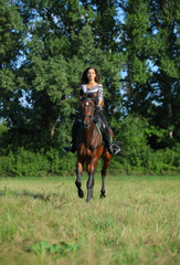Beautiful young woman riding a horse on the summer field