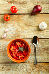 A plate of clay borscht with chicken with a spoon on a wooden table near vegetables.