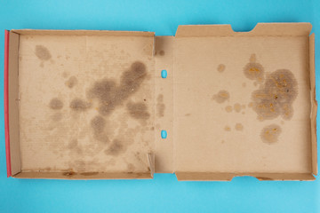 above view of greasy empty delivery pizza box on blue background