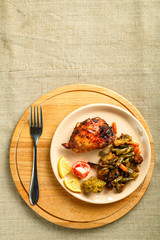 A plate with vegetables and a piece of chicken baked on a round stand on a wooden table with a fork.