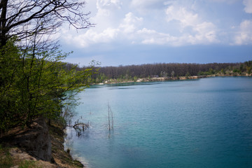 Happy and young girl and guy holding hands and laughing, on the background of a lake and a green meadow. A couple is standing in a meadow. Joyful summer day