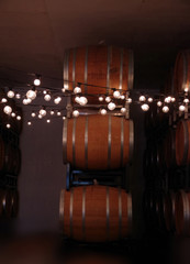 A chain of light bulbs sparely illuminating a dark room with a stack of wooden wine barrels
