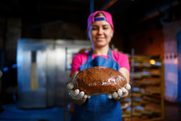 A baker girl takes hot bread in a bakery against the background of shelving with bread. Industrial...