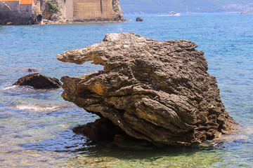 Relaxing on the nature. Tourism in Europe, ocean and sea vacations. Big rocks in the middle of the sea or ocean with great blue raging water waves breaking on a stone. Mogren Budva in Montenegro Beach