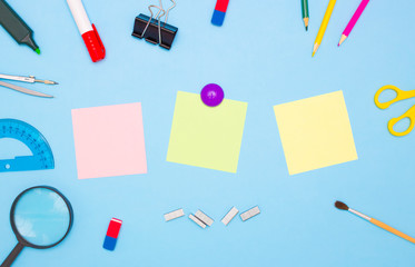 The concept of school and students. Three empty square of colored paper for notes in the middle. School and office stationery on the edges on a blue background. Top view, free space for text.