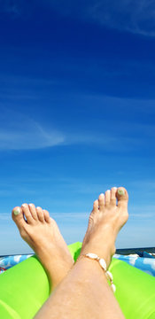 Pair of sun tanned feet with a seashell anklet and nail varnish over the blue sky