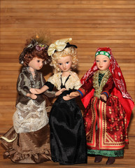 Three dolls in chic outfits on a wooden background.