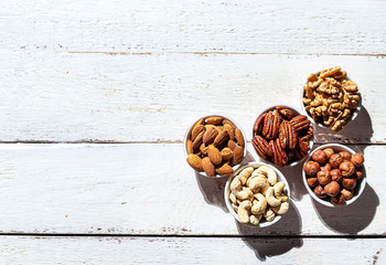 Various nuts in bowls on a white wooden background. Walnut, almonds, hazelnuts and cashews, pecans. Organic vegetarian food, healthy snacks.