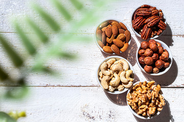 Various nuts in bowls on a white wooden background. Walnut, almonds, hazelnuts and cashews, pecans. Organic vegetarian food, healthy snacks.