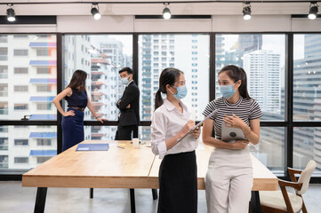 Young asian businesswoman colleague wearing face mask and talking in new normal office, Caucasian executive discussing on behind