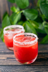 Refreshing cold red drink juice - freshly squeezed watermelon lemonade with ice. Bright juicy non-alcoholic cocktail on a dark wooden background. Idea for a homemade drink recipe. Selective focus