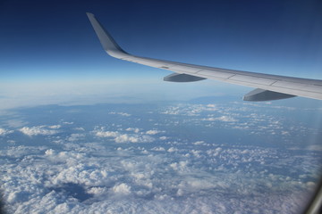 flying over clouds and the sea – looking out of a plane window, the left wing infront