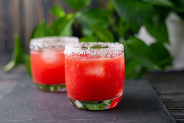 Refreshing cold red drink - freshly squeezed watermelon lemonade with ice. Bright juicy non-alcoholic cocktail on a dark wooden background. Idea for a homemade drink recipe. Selective focus