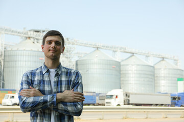 Young man against grain silos. Agriculture business © Atlas