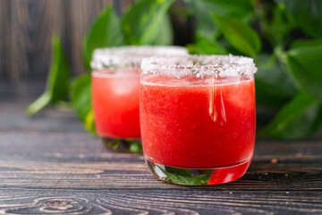 Refreshing cold red drink - freshly squeezed watermelon lemonade with ice. Bright juicy non-alcoholic cocktail on a dark wooden background. Idea for a homemade drink juice recipe. Selective focus