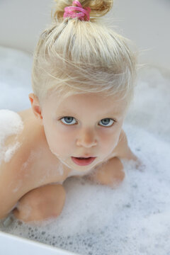 Blonde caucasian toddler girl bathing in a tub full of soap bubbles