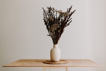 A bunch of wild dried flower in white ceramic vase closeup on brown wooden table