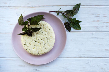 Fresh salted Levantine halloumi cheese and a sprig of basil on a pink plate on a white background. Traditional Cypriot cuisine.