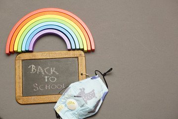 top view of blackboard with face mask with back to school message and rainbow. back to school concept with covid 19. flat lay. flat design