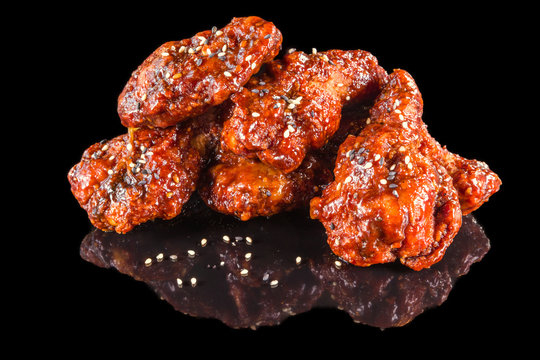 Delicious chicken wings with special marinade and sesame with reflection, isolated on black background