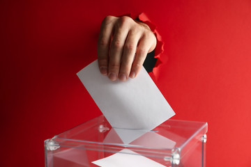 Man hand putting ballot into voting box on red background
