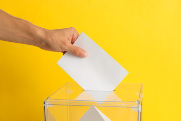 Man putting ballot into voting box on yellow background