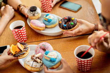 Close-up of group of friends eating donuts for dessert in a cafe.