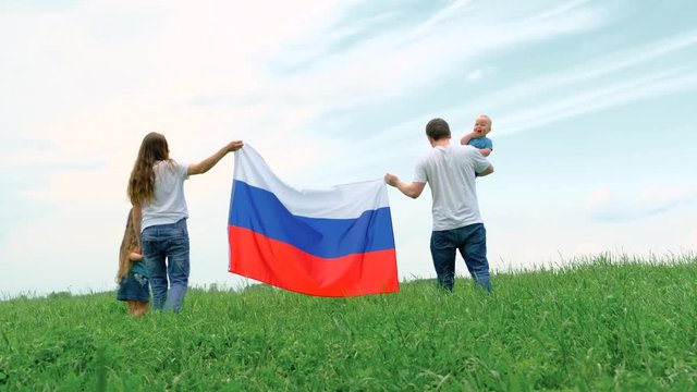 4k. Happy family mother father and two kids girl and little boy waving national Russia flag outdoors going on green grass blue sky at summer - russian flag, country, patriotism, Russia day.