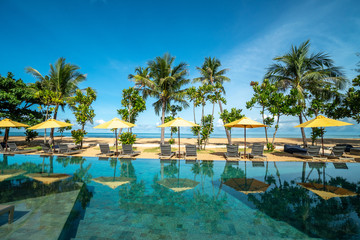 Beautiful luxury umbrella and chair around outdoor swimming pool in hotel and resort with coconut palm tree on blue sky