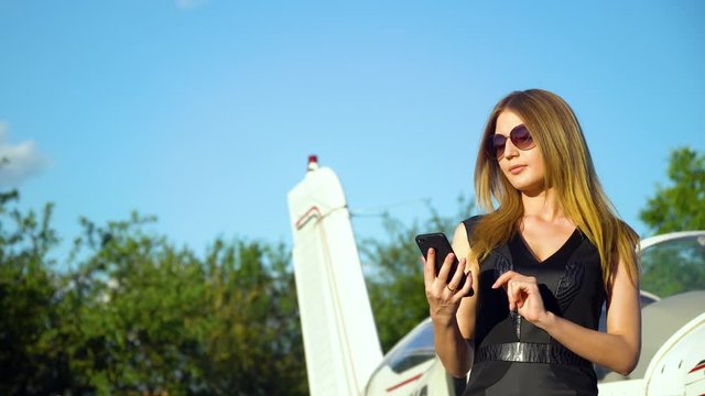 Businesswoman use smartphone in front of the parked small airplane plane