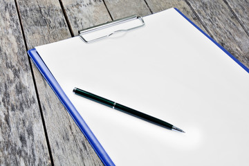 Clipboard with blank white paper and pen on a wooden table
