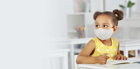 A dark-skinned girl in a medical mask and yellow dress in the school after covid