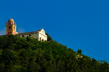 Fototapeta premium A small catholic church with a vibrant bell tower on a mountain covered with trees. This is a remote location in Liguria, Italy.