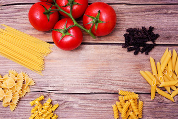 Tomatoes and different pasta on a wooden background