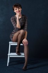 Fototapeta na wymiar a girl with short hair in a dress is sitting on a chair on a dark background.the woman smiles