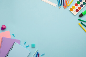 Obraz premium Top view of blue, pink and purple notebooks, pins, eraser, felt tip pens, color pencils, ruler, marker and watercolor. School stationery set on the blue background. Copy space. 