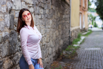 Beautiful young girl standing near the stone wall. Portrait pretty young fashion girl near a stone wall. Beautiful blonde woman with long hair posing near a stone wall.