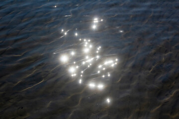 Glare in the wavy water of the lake from the rays of the sun. Background with waves on the surface of the lake.
