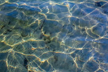 Fototapeta na wymiar Waves on the surface of the lake. Background with sun glare and waves. Transparent water in the reservoir. Sandy bottom of the lake.