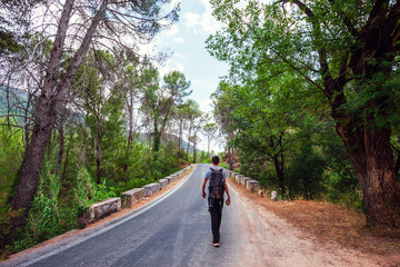 Young adventurer on his back with backpack walking while traveling on nature tourism on a road in the middle of the forest in the Cazorla Natural Park, in Spain. Selective focus.
