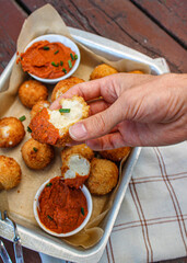 Deep-fried cheese balls with tomato sauce and chives in a baking tray as an appetizer. Hand dipping cheese balls into the sauce. 